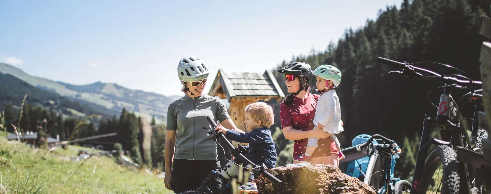 Familie mit Mountainbikes macht Pause vor Holzhäuschen in den Bergen