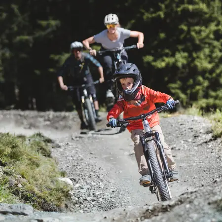 Familie fährt Mountainbike auf einem Waldweg, Kind im Vordergrund