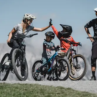 Familie mit Mountainbikes gibt sich High-Five vor Bergpanorama