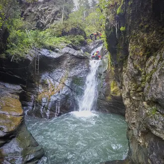 Canyoning: Wasserfall in Felsenschlucht, Person mit rotem Helm seilt sich ab