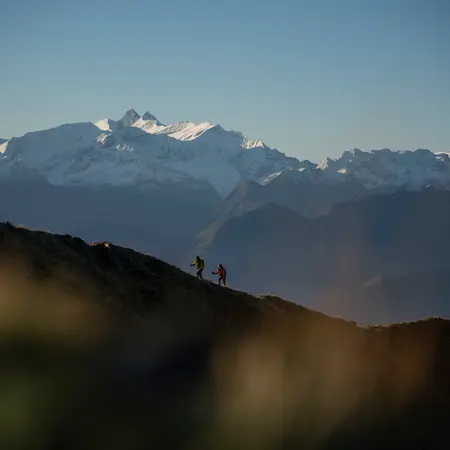 Zwei Wanderer auf Bergkamm vor schneebedeckten Gipfeln