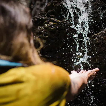 Hand berührt Wasserfall im Wald