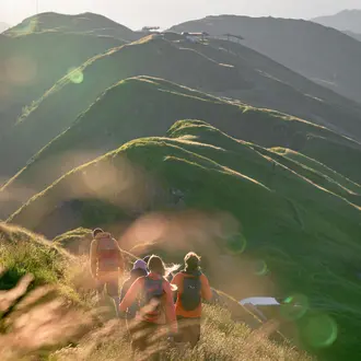 Wandergruppe auf einem grasbewachsenen Bergrücken mit Blick auf weitere Berge im Gegenlicht