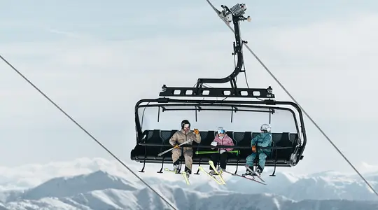 Skifahrer in Sessellift vor verschneiter Berglandschaft