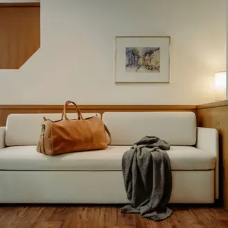 Helle Couch mit Reisetasche und Decke vor Wand mit Bild