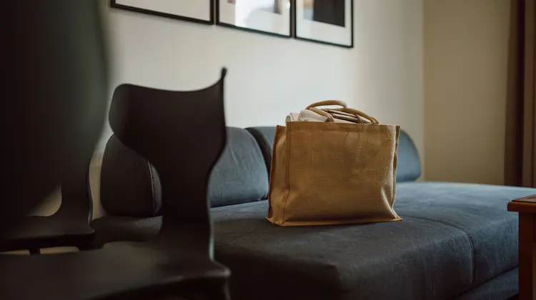 Brown fabric bag on blue sofa, black chair in the foreground, pictures on the wall