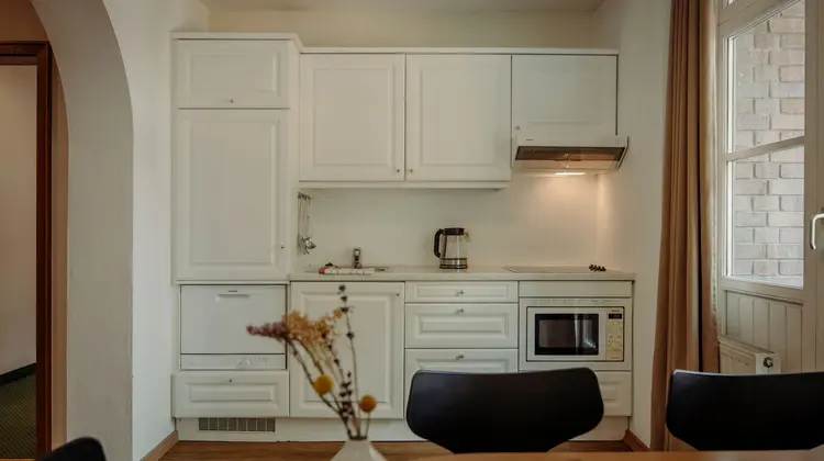 Small kitchenette with white cabinets, sink, microwave and kettle