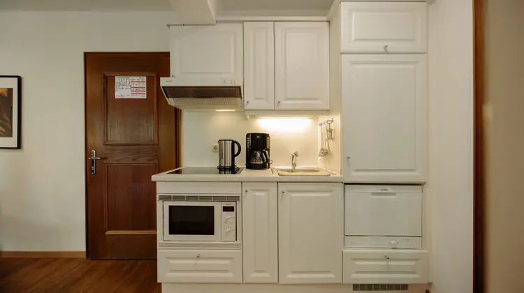 Small white kitchenette with sink, stove, microwave and cupboards