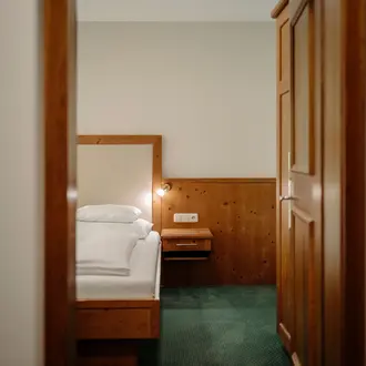 Blick durch Türrahmen auf ein Hotelzimmer mit Bett, Nachttisch und Schrank