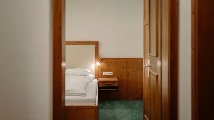 View through door frame into a hotel room with bed, bedside table and wardrobe