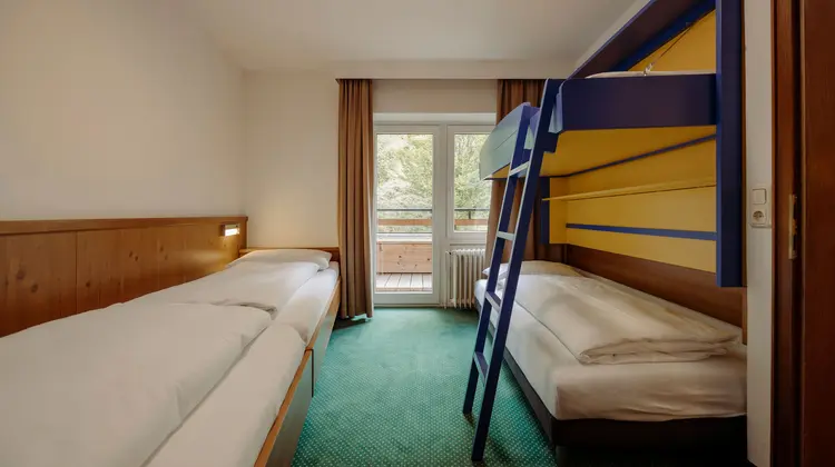 Room with single bed, bunk bed, green carpet and balcony door