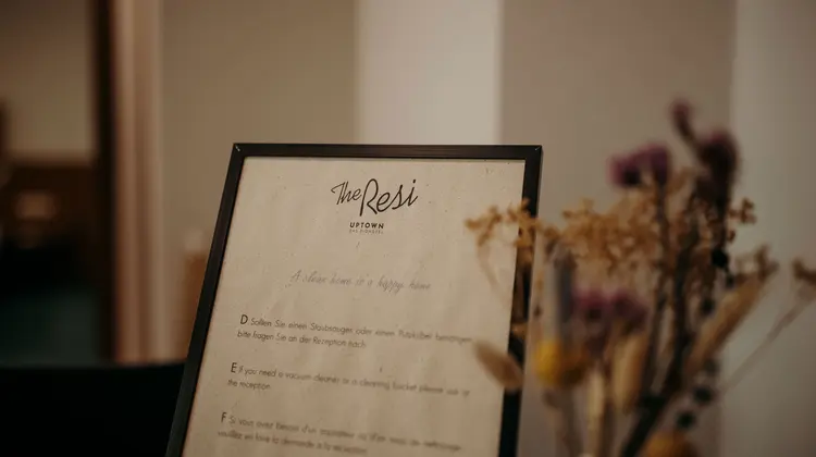 Sign with text "The Resi Uptown" and rules next to dried flowers