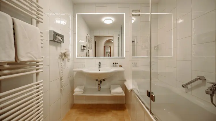 Helles Badezimmer mit Waschbecken, Spiegel, Handtüchern und Badewanne mit Glaswand