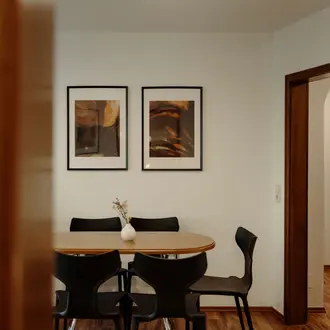 Esszimmer mit Holztisch, schwarzen Stühlen und zwei gerahmten Bildern an der weißen Wand
