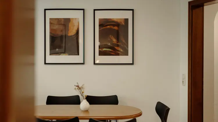 Esszimmer mit Holztisch, schwarzen Stühlen und zwei gerahmten Bildern an der weißen Wand