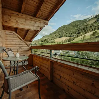 Holzbalkon mit Tisch und Stühlen vor Berglandschaft