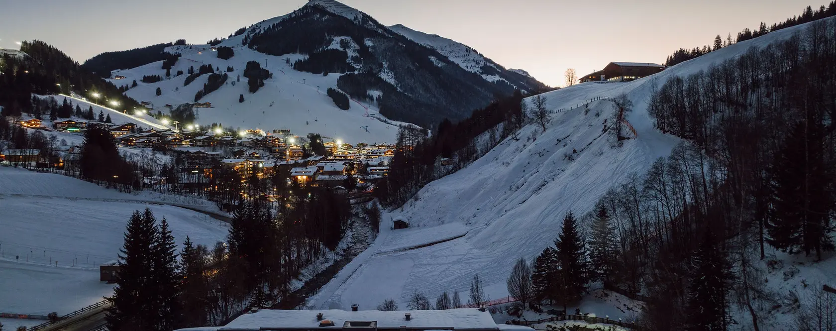 Winterliche Berglandschaft mit Schnee, Häusern und beleuchtetem Pool im Vordergrund