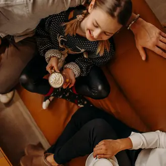 Mädchen sitzt mit Kakao auf Couch, lächelt, umgeben von Erwachsenen