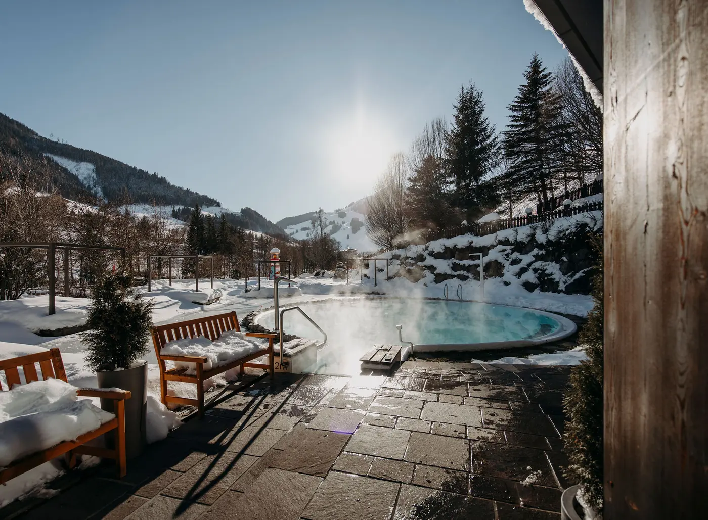 Beheizter Außenpool des Gartenhotel Theresia mit Dampf und Schnee vor Bergkulisse