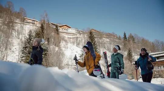 Gruppe junger Leute mit Skiern und Snowboard im Schnee vor Bergkulisse