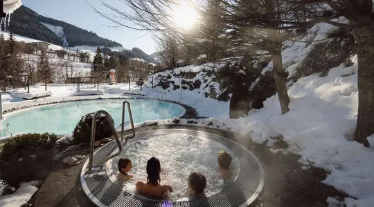 Winterlandschaft mit dampfendem Whirlpool und Badenden im Vordergrund
