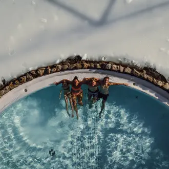 Three people lying in the round pool, surrounded by snow