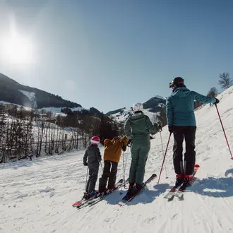 Familie steht auf Ski auf einer schneebedeckten Piste mit Bergen im Hintergrund