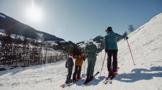 Familie steht auf Ski auf einer schneebedeckten Piste mit Bergen im Hintergrund