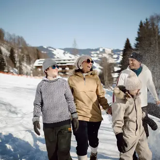 Familie mit zwei Kindern spaziert im Winter durch eine verschneite Landschaft