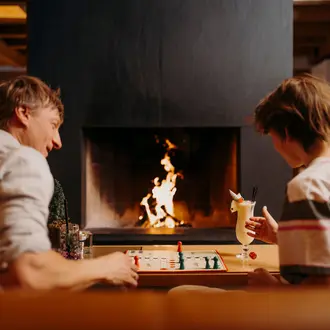 Vater und Sohn spielen ein Brettspiel, vor dem Kamin in der Hotellobby.