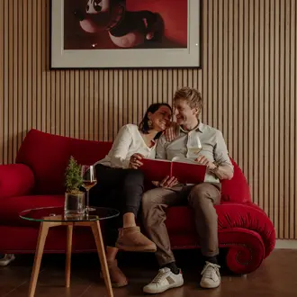 Paar sitzt auf rotem Sofa, hält Album, Wein auf Tisch