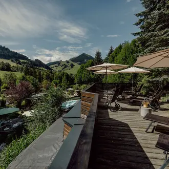 Holzterrasse mit Liegen und Sonnenschirmen vor grüner Hügellandschaft
