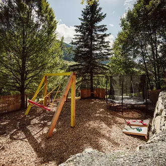 Spielplatz mit Schaukel, Trampolin und Holzzaun im Grünen