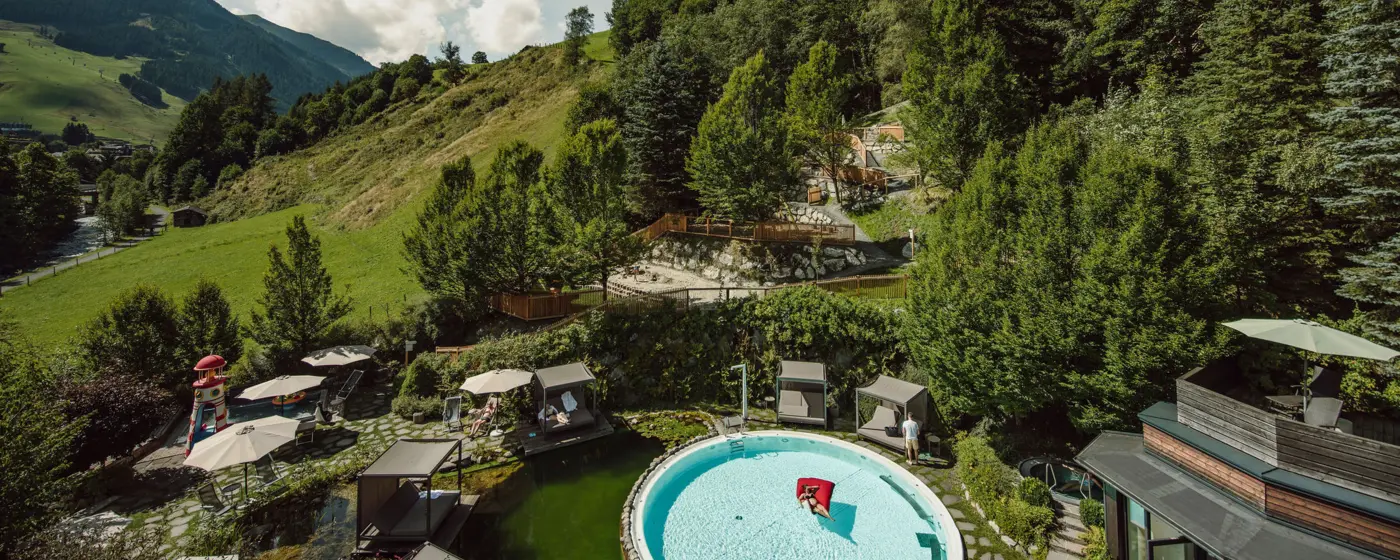 Poolanlage vor bewaldetem Berghang an sonnigem Tag