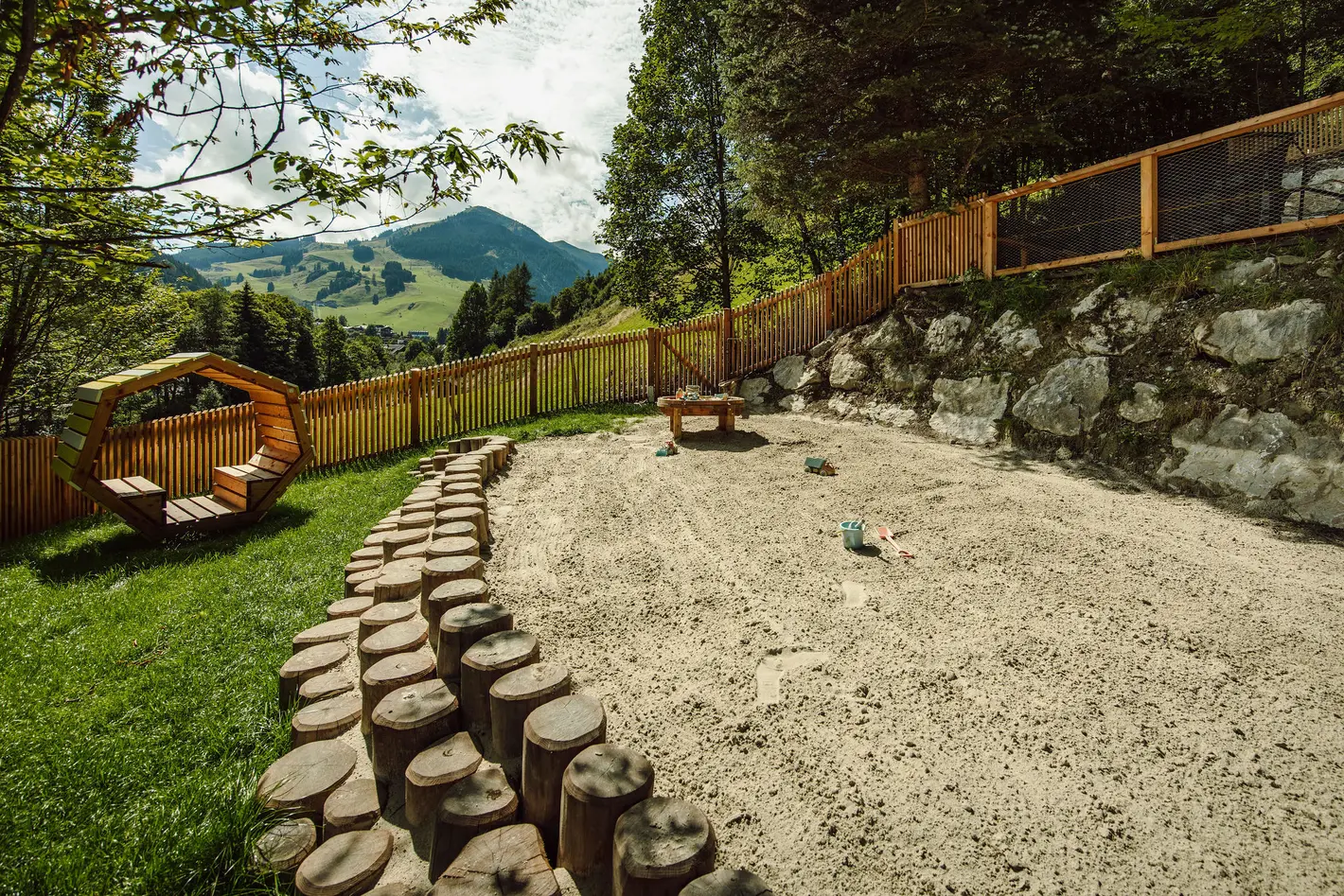 Playground with wooden fence, tree trunks as a path and mountain panorama in the background