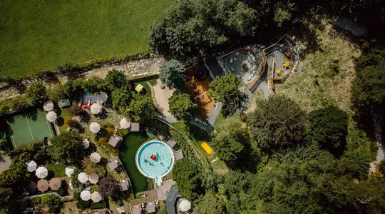 Draufsicht auf Schwimmbad mit runden Becken, umgeben von Bäumen und Grünflächen