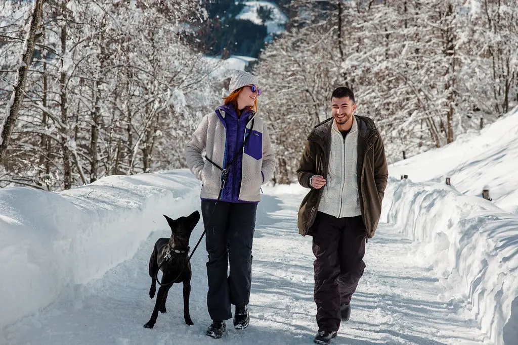 Paar mit Hund wandert im Winter durch verschneite Landschaft