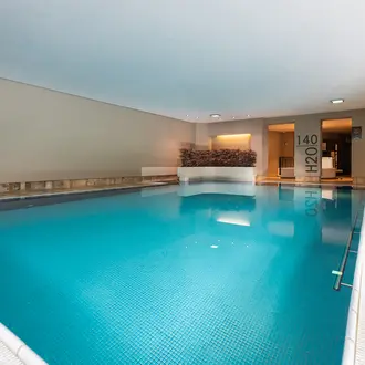 Innenpool mit blauem Wasser, Fliesenboden und Pflanzenwand