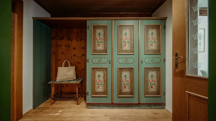 Alter Bauernschrank mit Blumenmalerei neben Sitzecke mit Tasche im rustikalen Zimmer