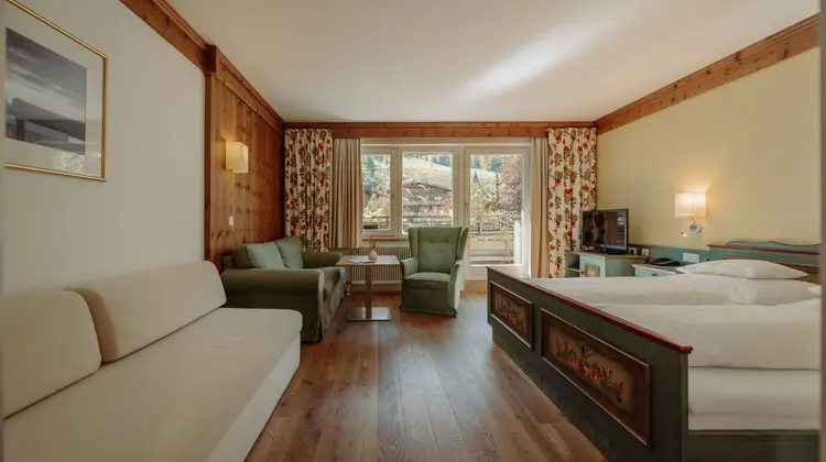 Hotelzimmer mit Sofa, Sessel, Bett und Fenster mit Blick ins Grüne