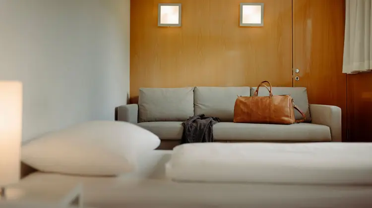 Helles Zimmer mit Sofa, Reisetasche und zwei Wandlampen