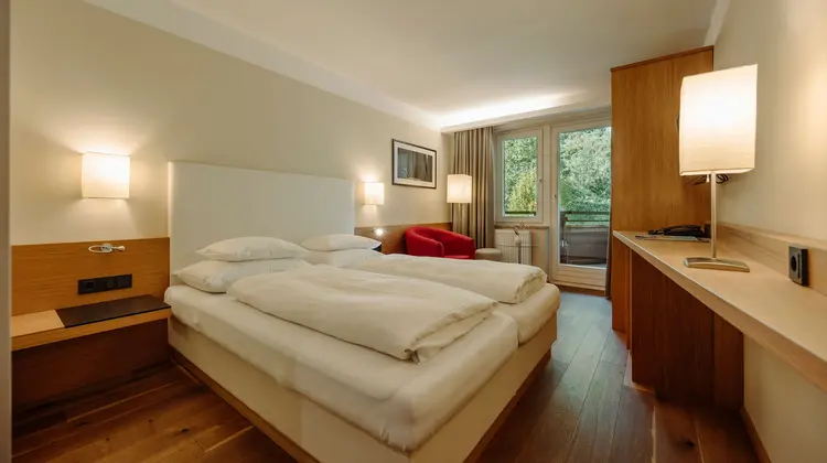 Hotelzimmer mit Doppelbett, rotem Sessel und Balkon