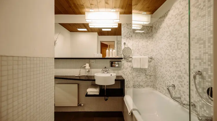 Badezimmer mit Waschbecken, Badewanne, Spiegel und Decke aus Holz