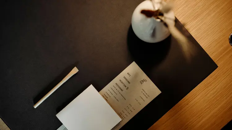 Tisch mit Speisekarte, Notizzettel, Vase und Strohhalm von oben