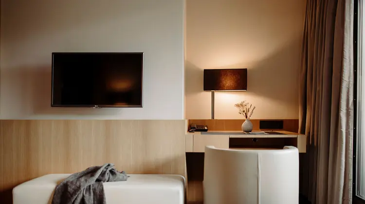 Hotelzimmer mit Fernseher, Schreibtisch, Lampe, Sessel und Couch