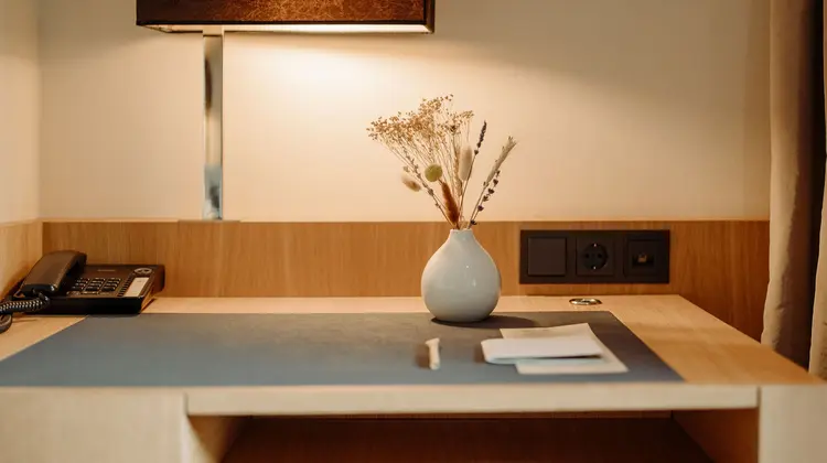 Schreibtisch mit Lampe, Telefon, Vase mit Trockenblumen und Papier vor heller Wand