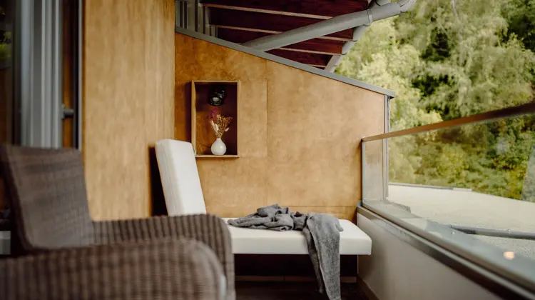 Balkon mit Liege, Sessel, Blumen in Vase und Holzwand