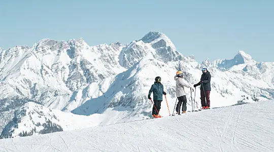 Drei Skifahrer auf schneebedecktem Hang vor Bergpanorama unter blauem Himmel